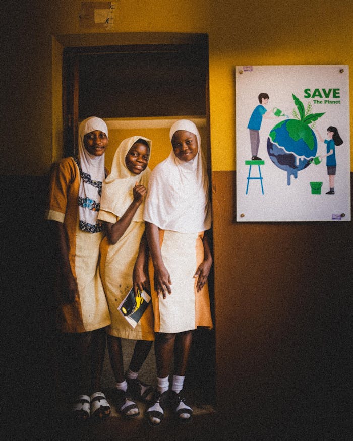 about-01 Three schoolgirls in uniform pose beside an environmental poster indoors.